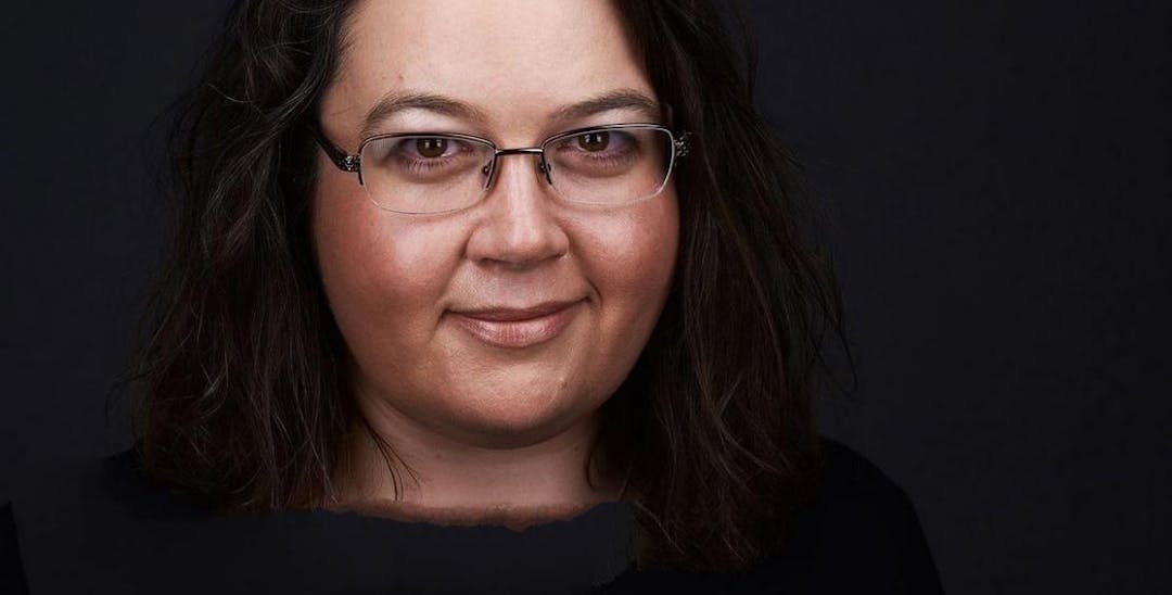 A close-up photo of Claire Victory with a black background. She has dark hair and wears glasses.
