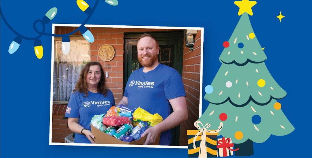 An image with a blue background and a photo of 2 Vinnies WA volunteers holding a box of food donations. Next to the photo is a graphic of a decorated Christmas tree and 2 Christmas presents underneath the tree.