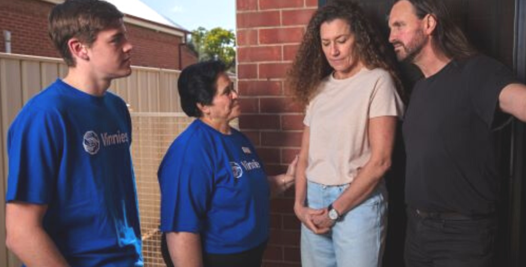 A photo of 4 people talking on the doorstep of a house. 2 of the people are in blue Vinnies t-shirts, the other 2 in casual wear. They are talking to each other. 