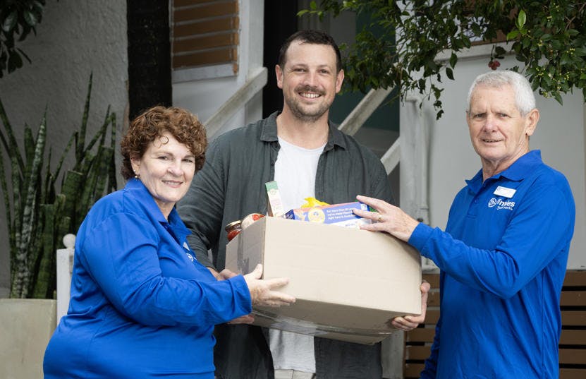 2 men and a woman holding a box of food. One man and the woman are wearing Vinnies blue tshirts. They are all smiling and facing the camera.