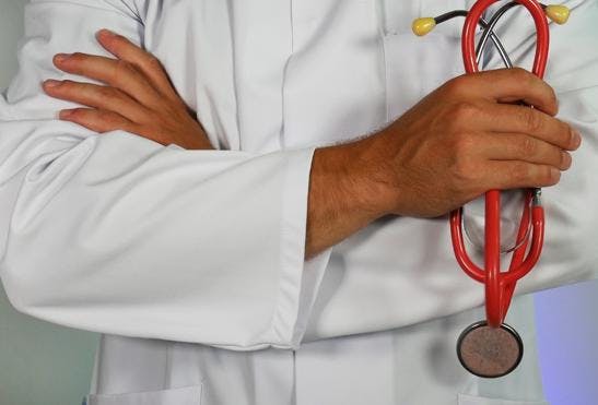A photo of a torso in a white coat and arms crossed holding a red stethoscope.