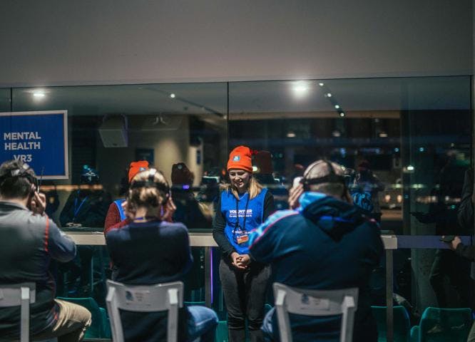 A photo of several young people wearing beanies and virtual reality glasses in a room. 2 of them are wearing Vinnies vests over their clothes.