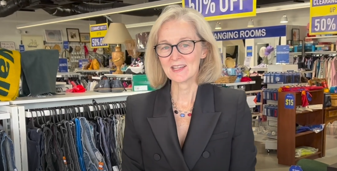 A photo of the Chief Executive Director Susan Rooney at a Vinnies WA shop. She is centre of the photo with clothes racks and clearances signs in the background. She is facing the camera while talking.