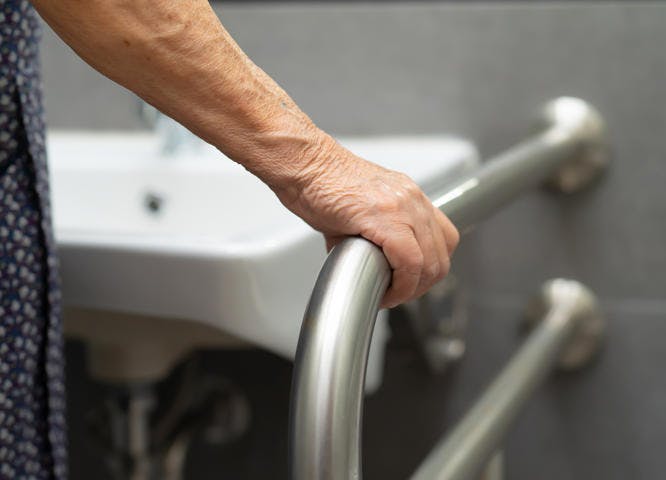 Elderly woman holding onto support bar in bathroom