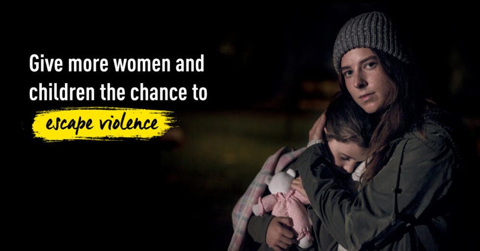 An photo of a mother holding her child while she is looking into the camera. To the left is the text "Give more women and children the chance to escape violence".