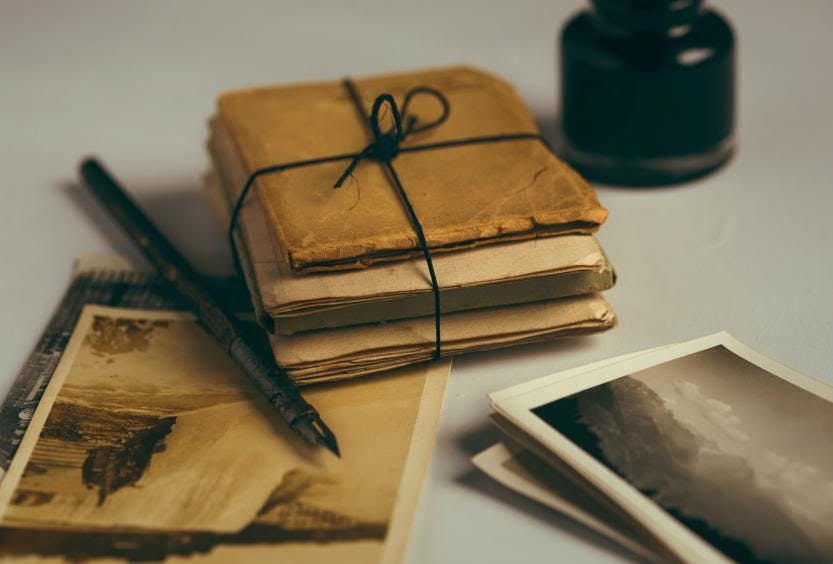 A photo of a stack of old papers, envelopes and photos bound up next to a fountain pen and ink.