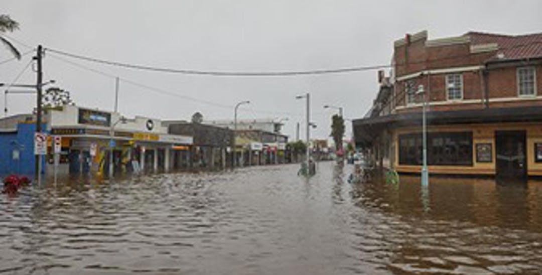 A photo of a street in Lismore with buildings on each side and murky water up to the windows, looks like a river.