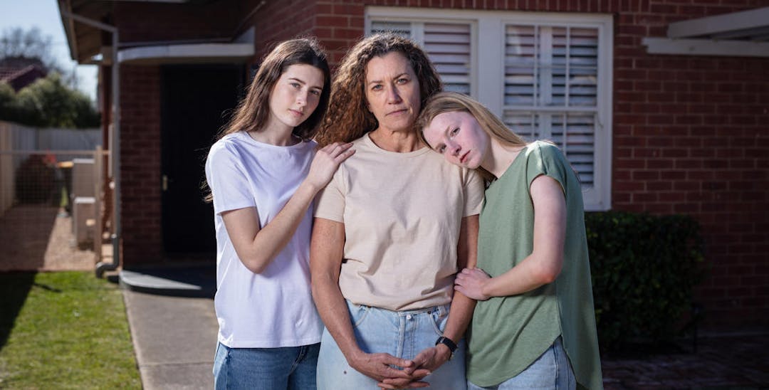 A photo of a struggling family consisting of two teenaged daughters hugging their mother and looking into the camera.