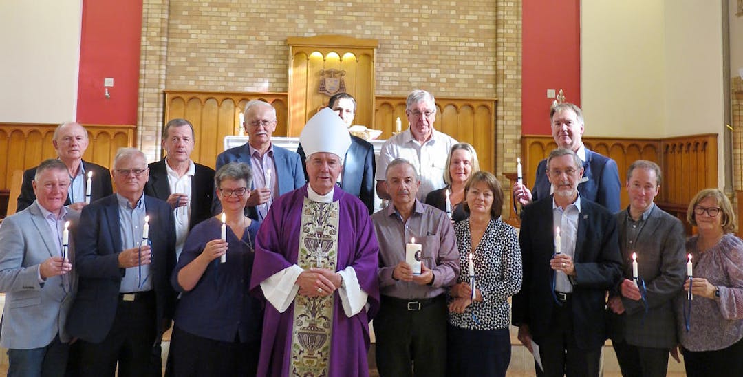 A group of people standing in a church facing the camera each holding a candle.