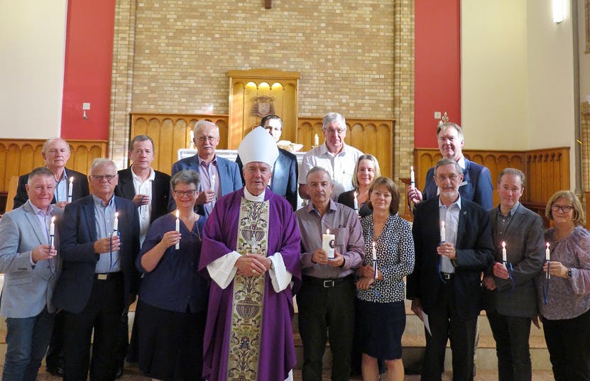 A group of people standing in a church facing the camera each holding a candle.