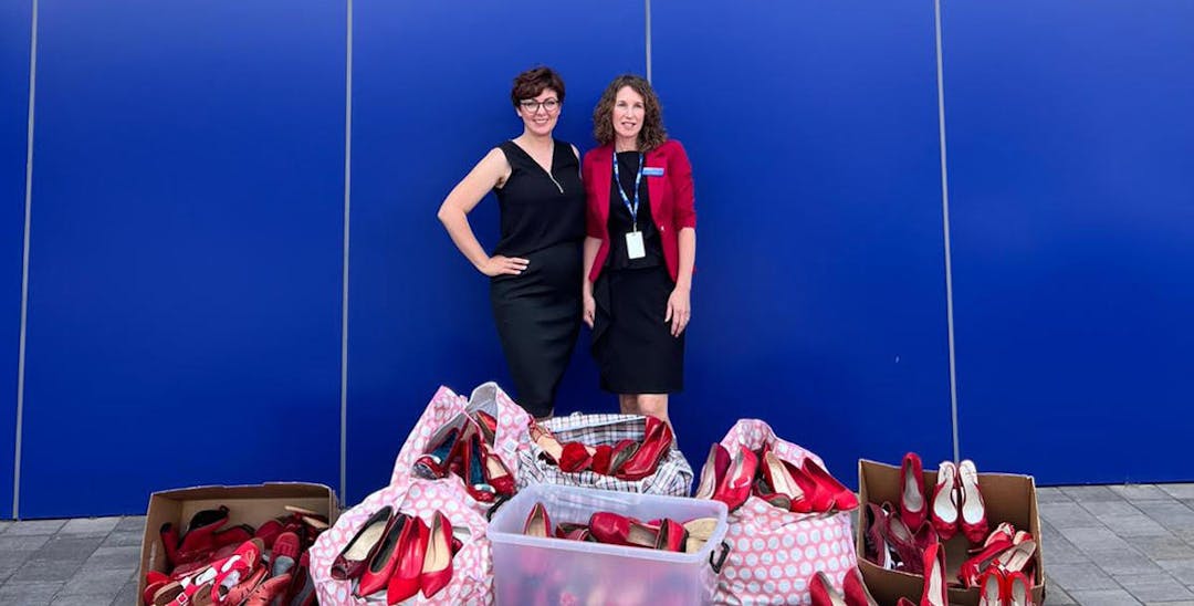 A photo of forensic scientist and justice campaigner, Dr Paola Magni, together with Vinnies WA staff standing behind a pile of donated red womens' shoes