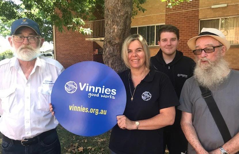 A group of people smiling and posing together with a 'Vinnies Good Works' sign.