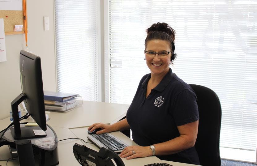 A woman sitting at a desk smiling with a headset on, taking Helpline calls.