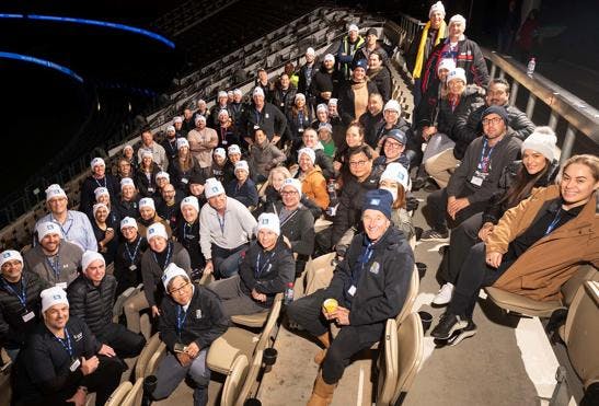 A photo of a sitting crowd of approximately 70 people during night time at the Optus Stadium. Everyone is wearing either Vinnies WA CEO Sleepout hats or lanyards and smiling at the camera. 
