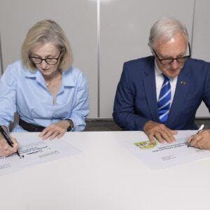 A photo of Chief Executive Officer Susan Rooney and State President David Kennedy sitting besides each other at a table and signing documents. They are both looking down at their own paper.
