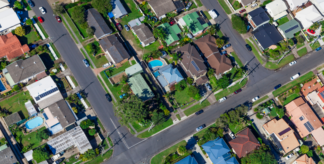 An aerial photo of a suburb with house roofs and streets and some greenery.