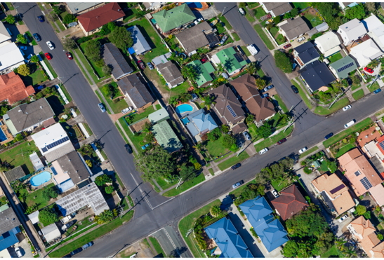 An aerial photo of a suburb with house roofs and streets and some greenery.