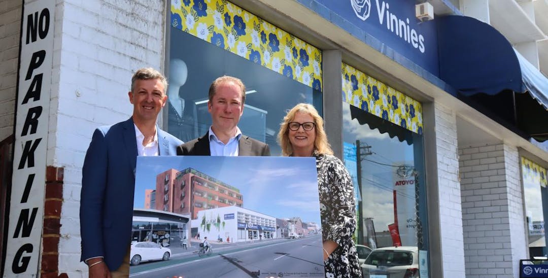 2 men and a woman holding a picture of a building and standing in front of a Vinnies shop.