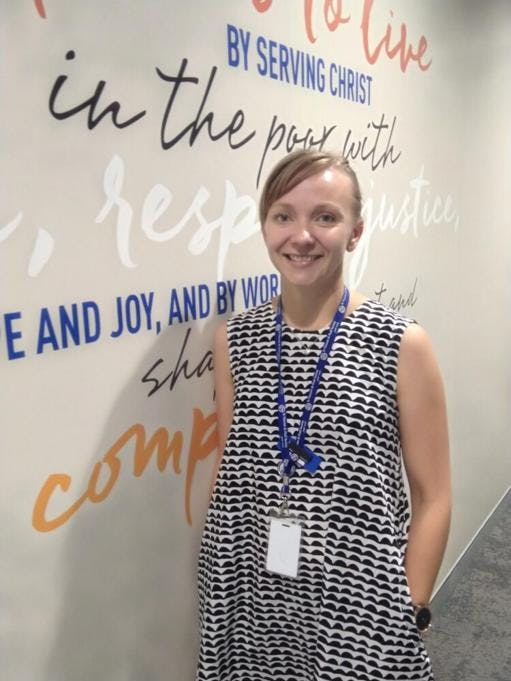 A photo of Manager of Service Development, Maija Hildebrand standing next to a wall filled with quotes. She is facing the camera and smiling.