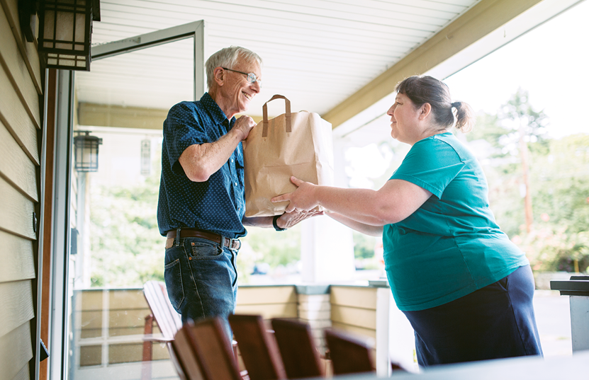 A woman (conference member) kindly offers a bag of groceries to a man (companion).