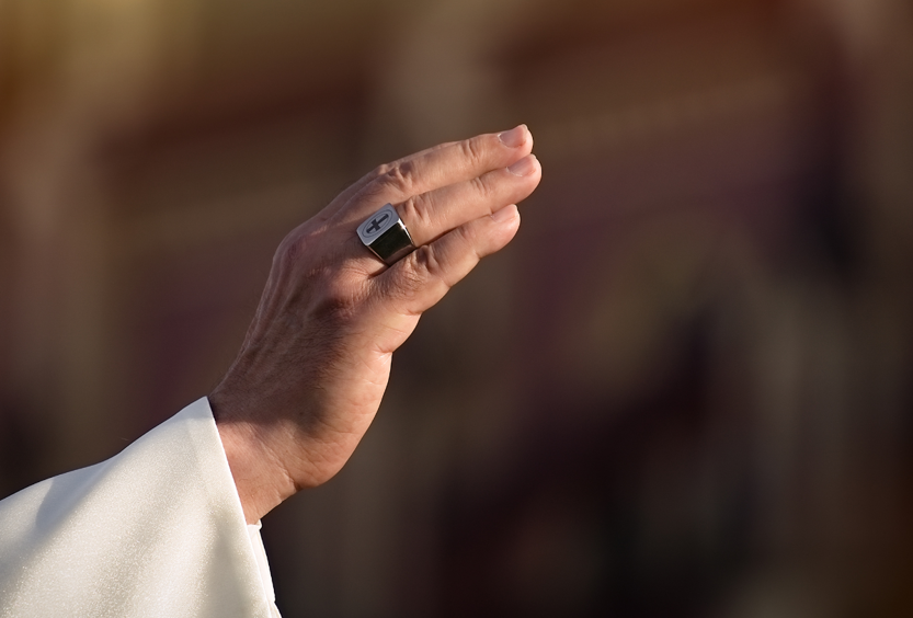 A photo of a close up of a hand wearing a ring with a cross, as in a blessing.